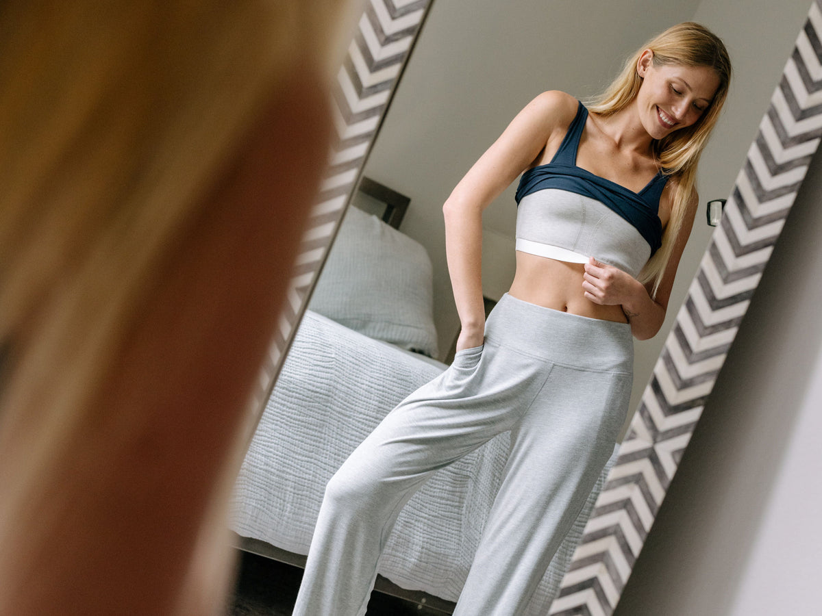 A woman posing in front of a mirror wearing breathable cooling pajamas for hot sleepers - gray pants and a blue crop top with a built-in bra.
