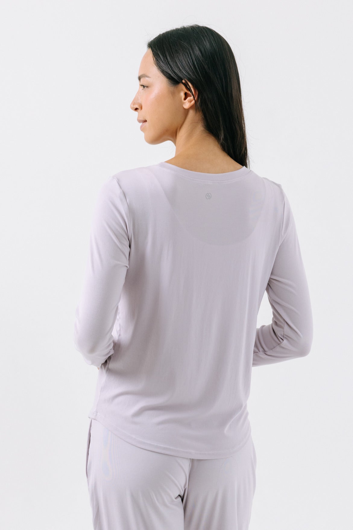 A woman showing the back of a lavender, long-sleeve pajama t-shirt on a white studio background.