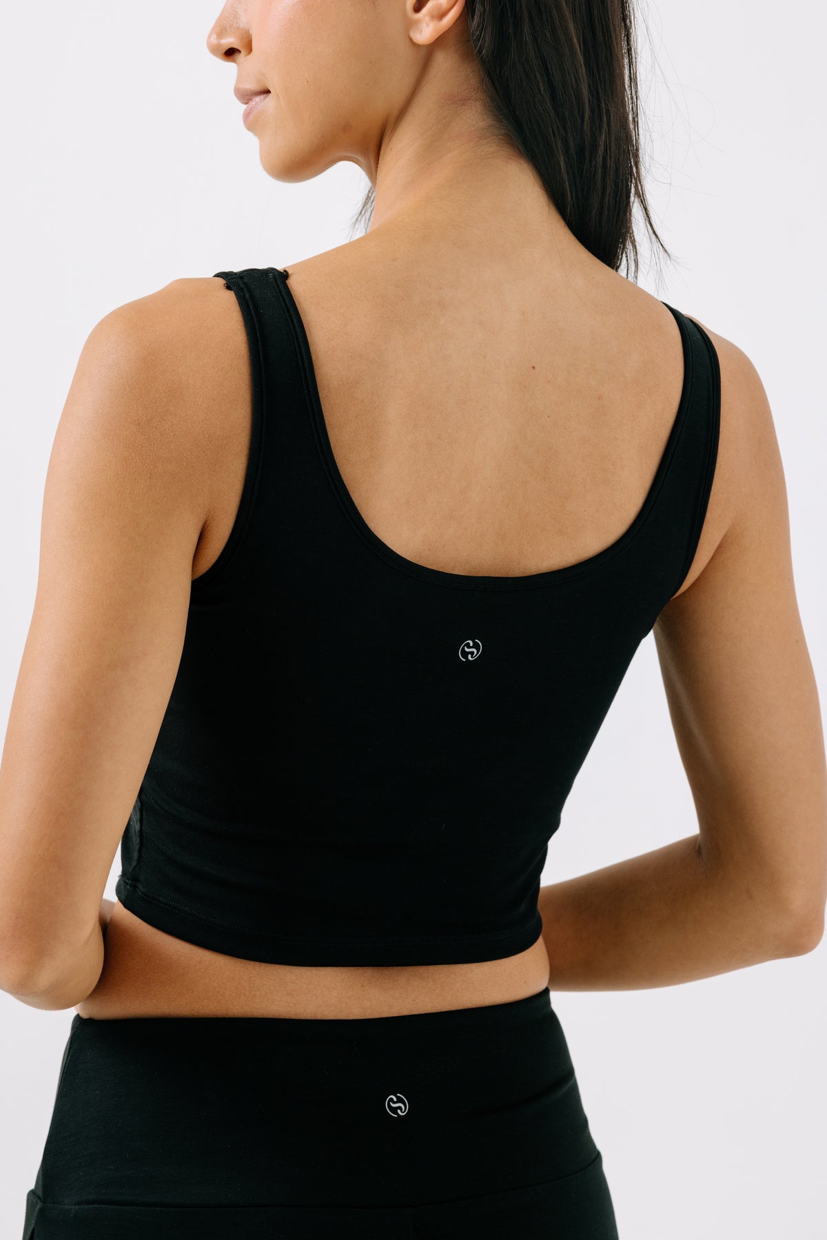 Woman showing the back of a black pajama crop top on a white studio background.