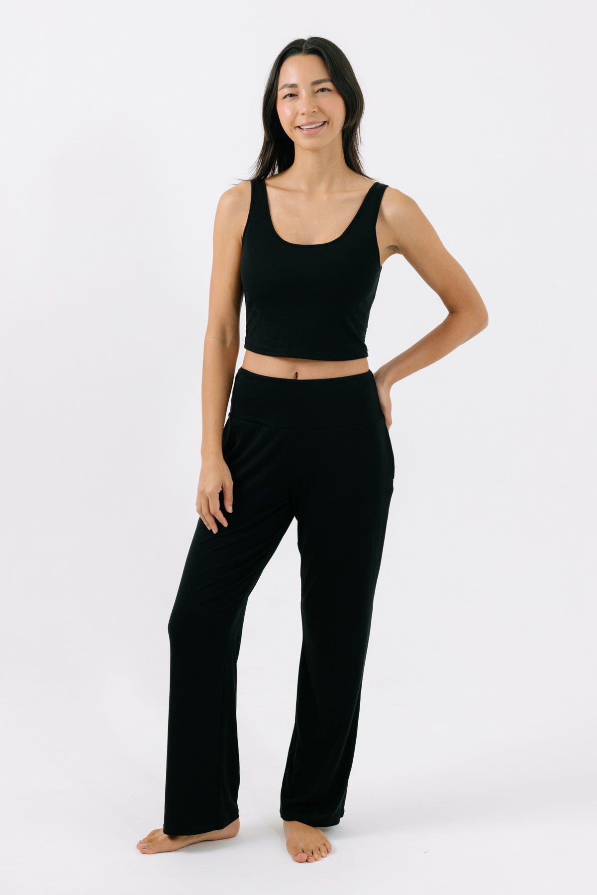 Woman wearing a black pajama crop top and matching black pajama pants on a white studio background.
