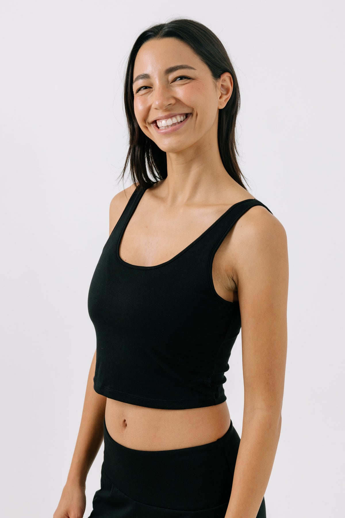 Woman smiling and wearing a black pajama crop top on a white studio background.