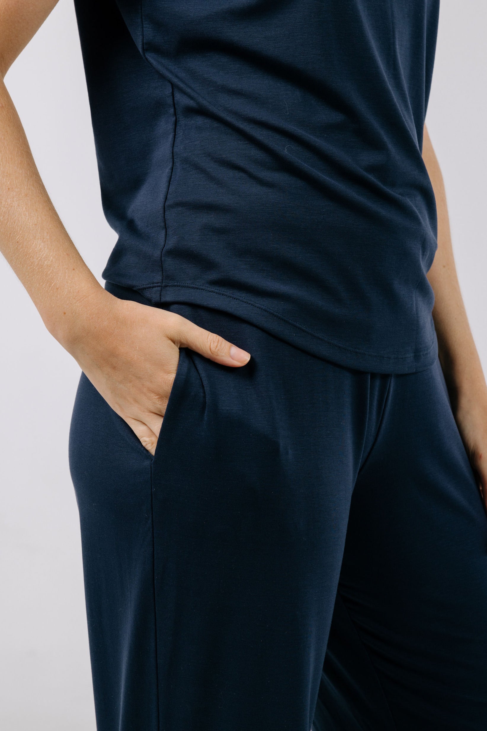 Person wearing a navy blue pajama t-shirt and pants with hands in pockets on a plain background.