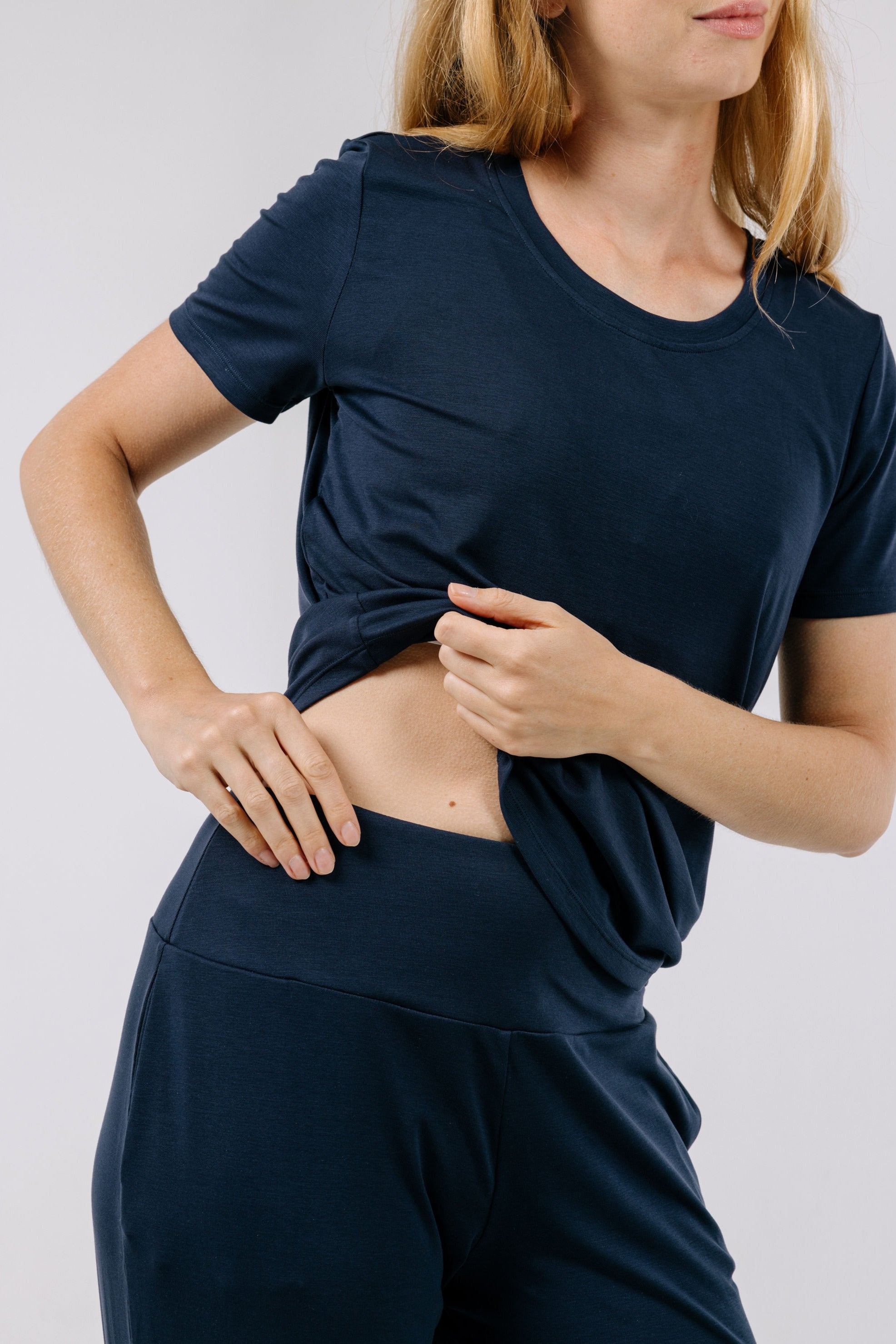 Woman wearing a navy blue pajama t-shirt and matching pants on a plain background.