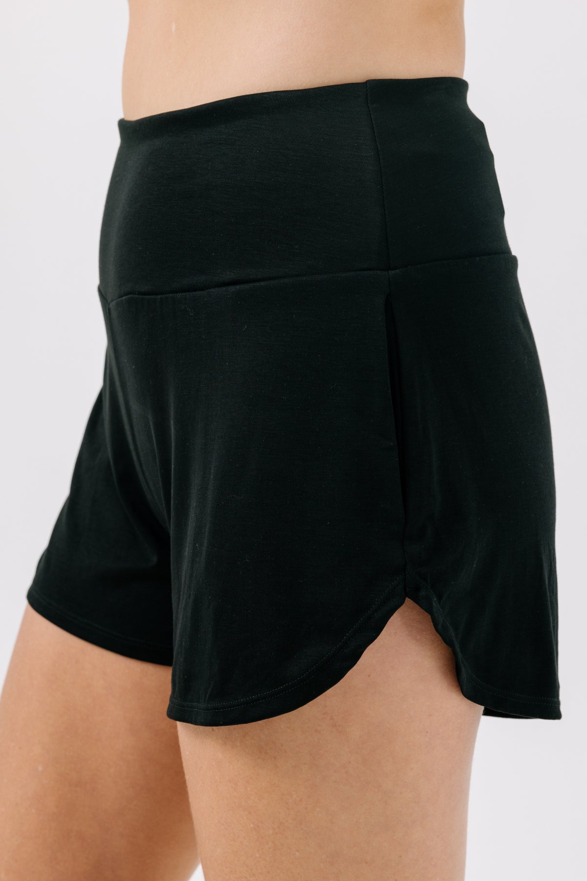 Woman wearing sporty black pajama shorts on a white studio background.