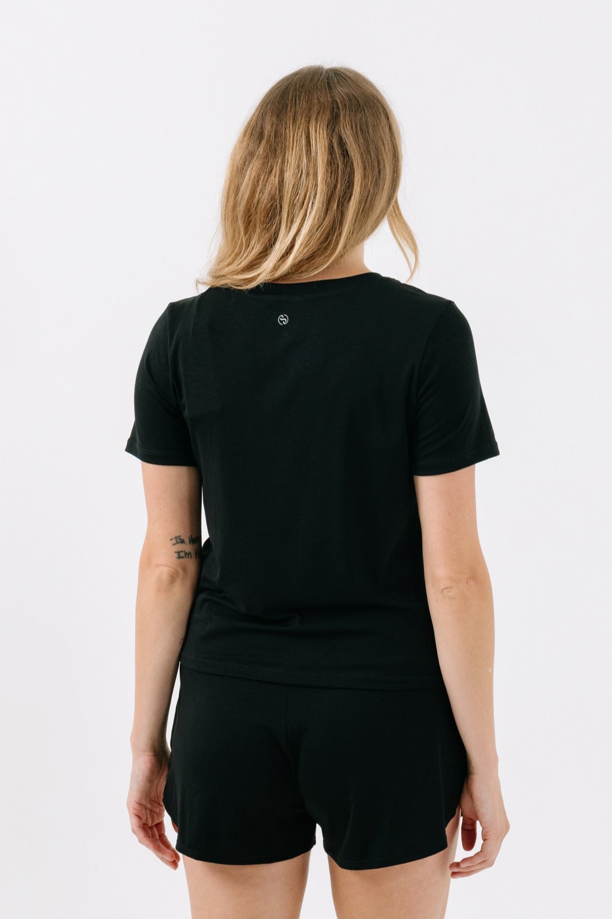 Woman showing the back of a black pajama t-shirt on a white studio background.