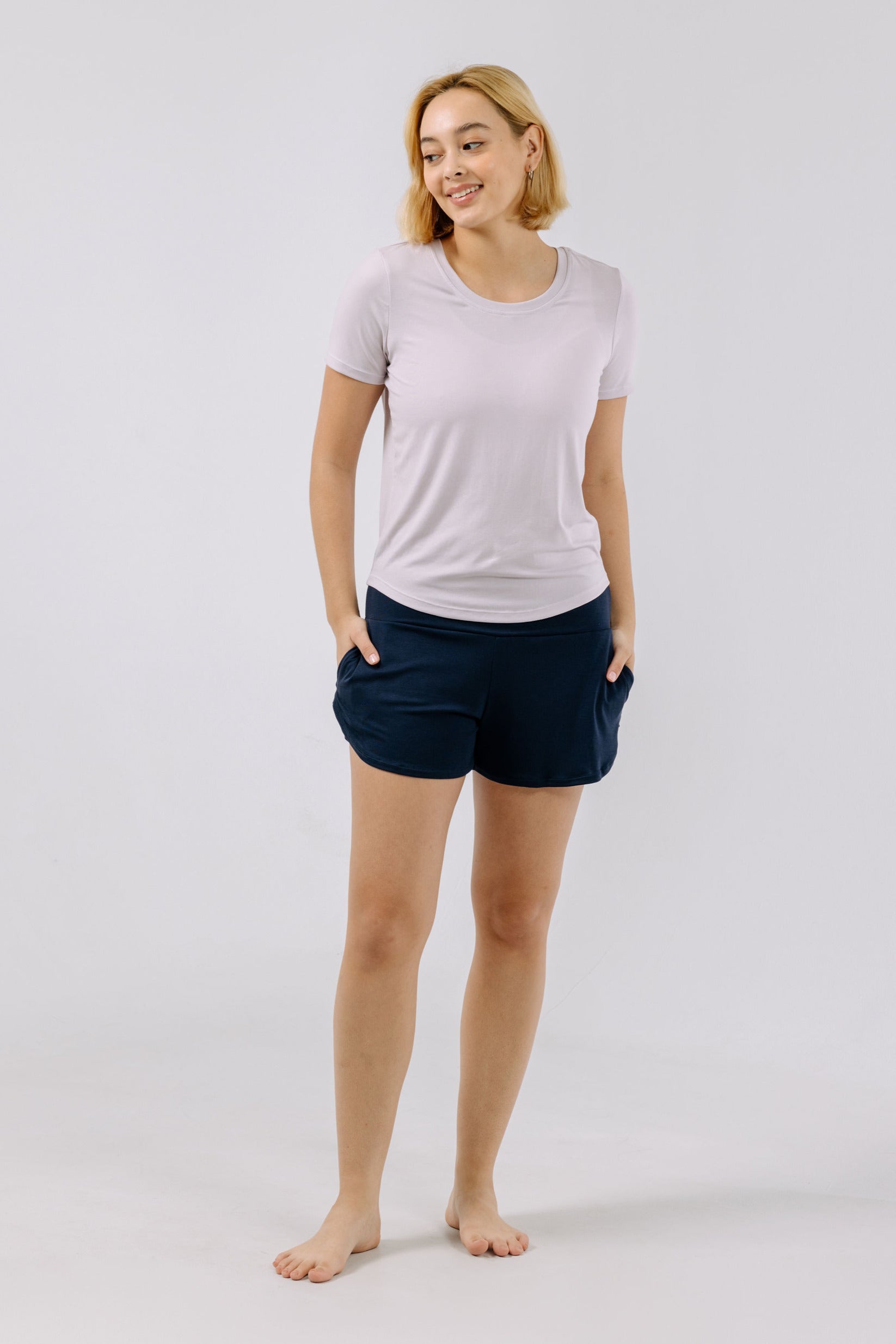 Woman wearing a lavender pajama t-shirt and navy shorts on a white background.