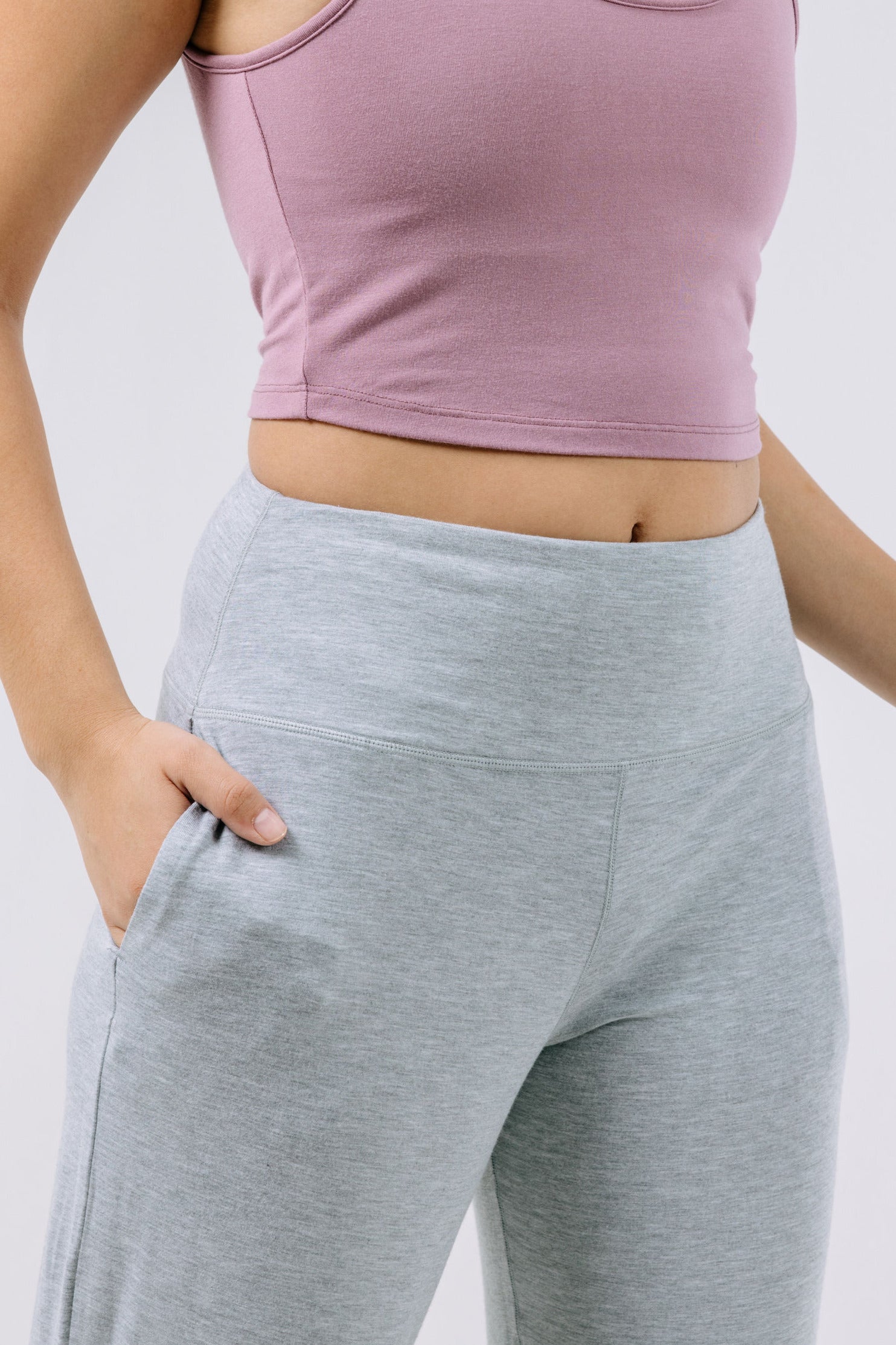 Person wearing a lavender pajama crop top and gray pants on a white background.
