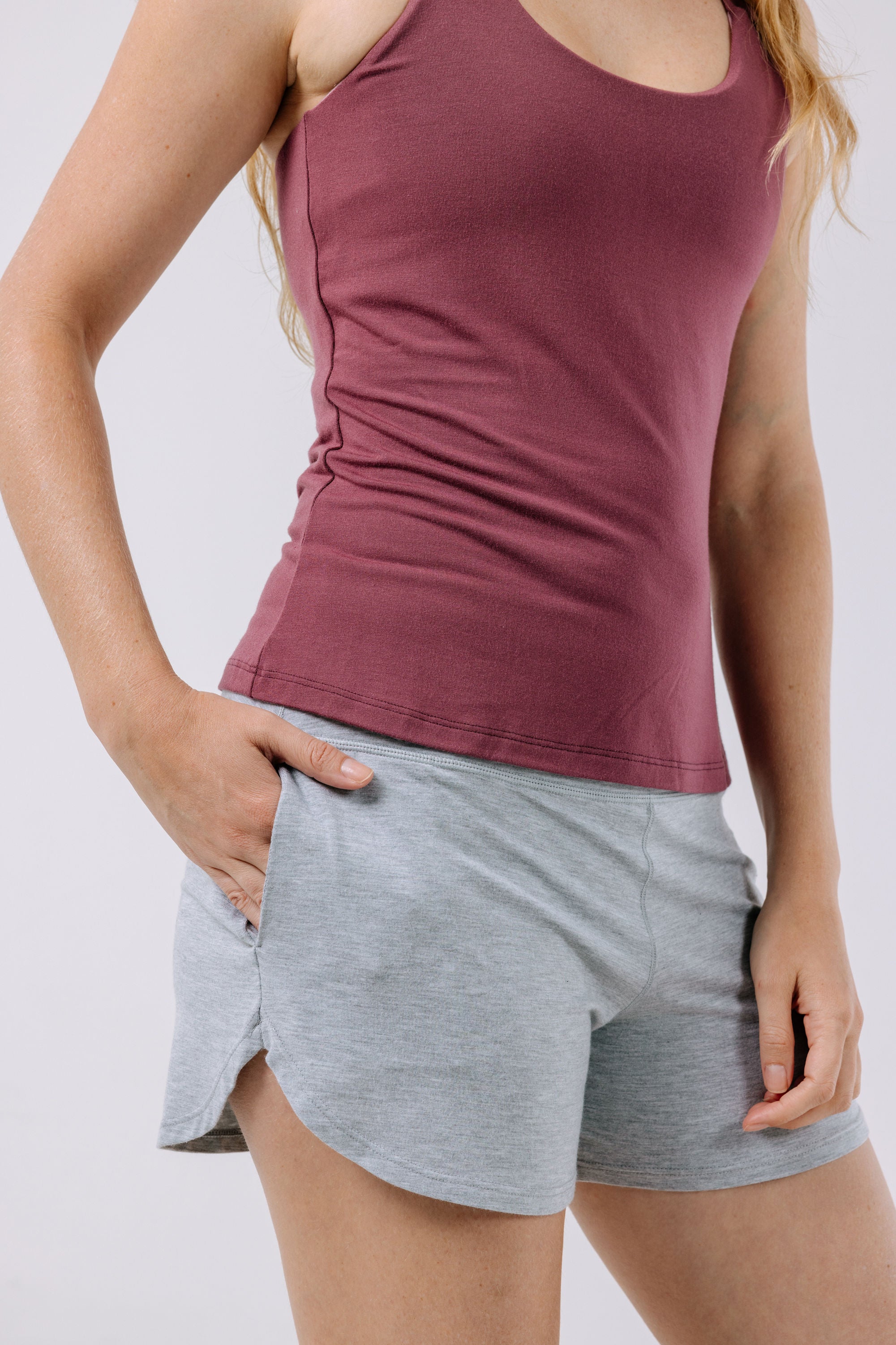 Person wearing a plum pajama tank top and gray shorts with pockets on a white background.