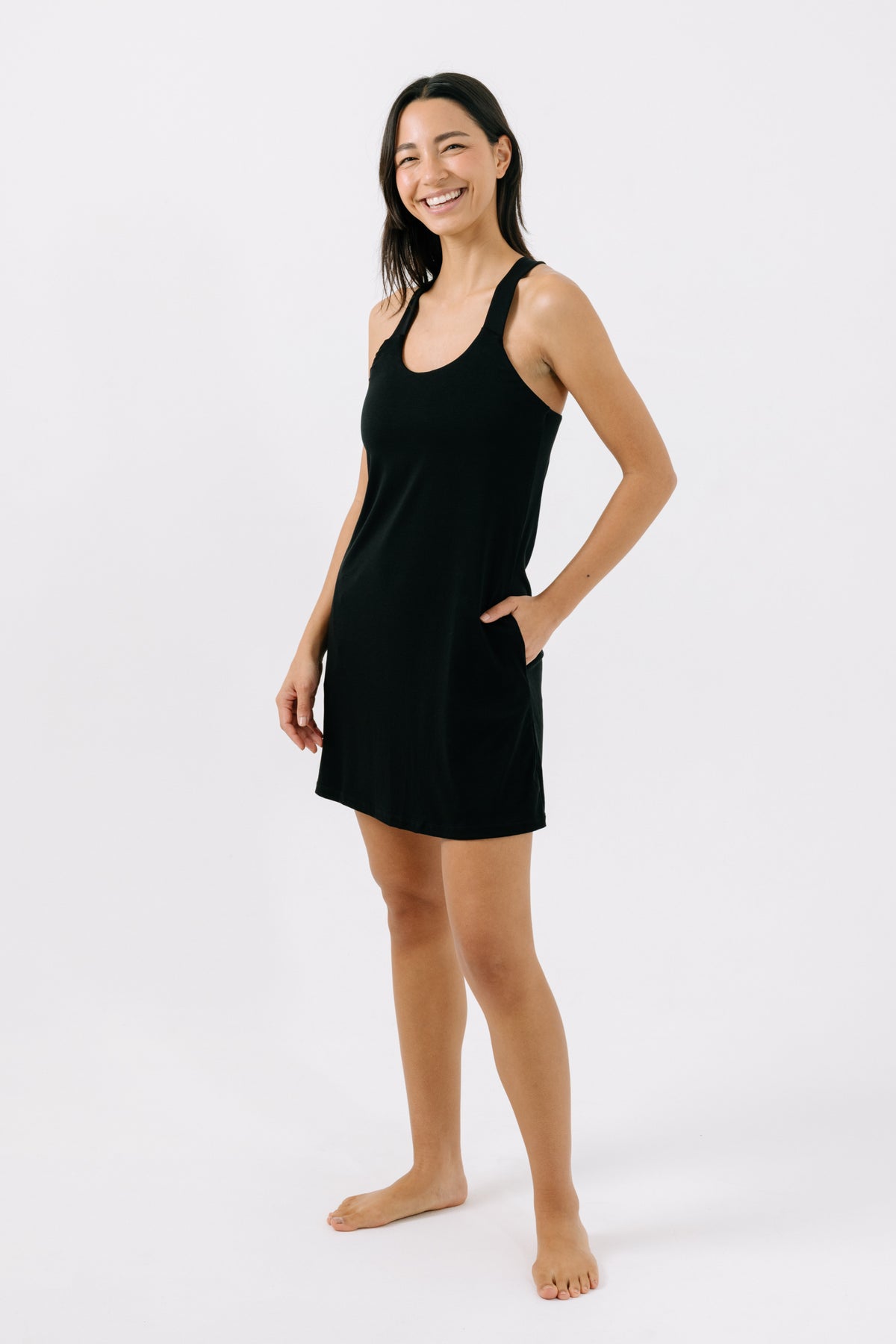 Woman wearing a black racerback pajama dress with her hand in her pocket on a white background.