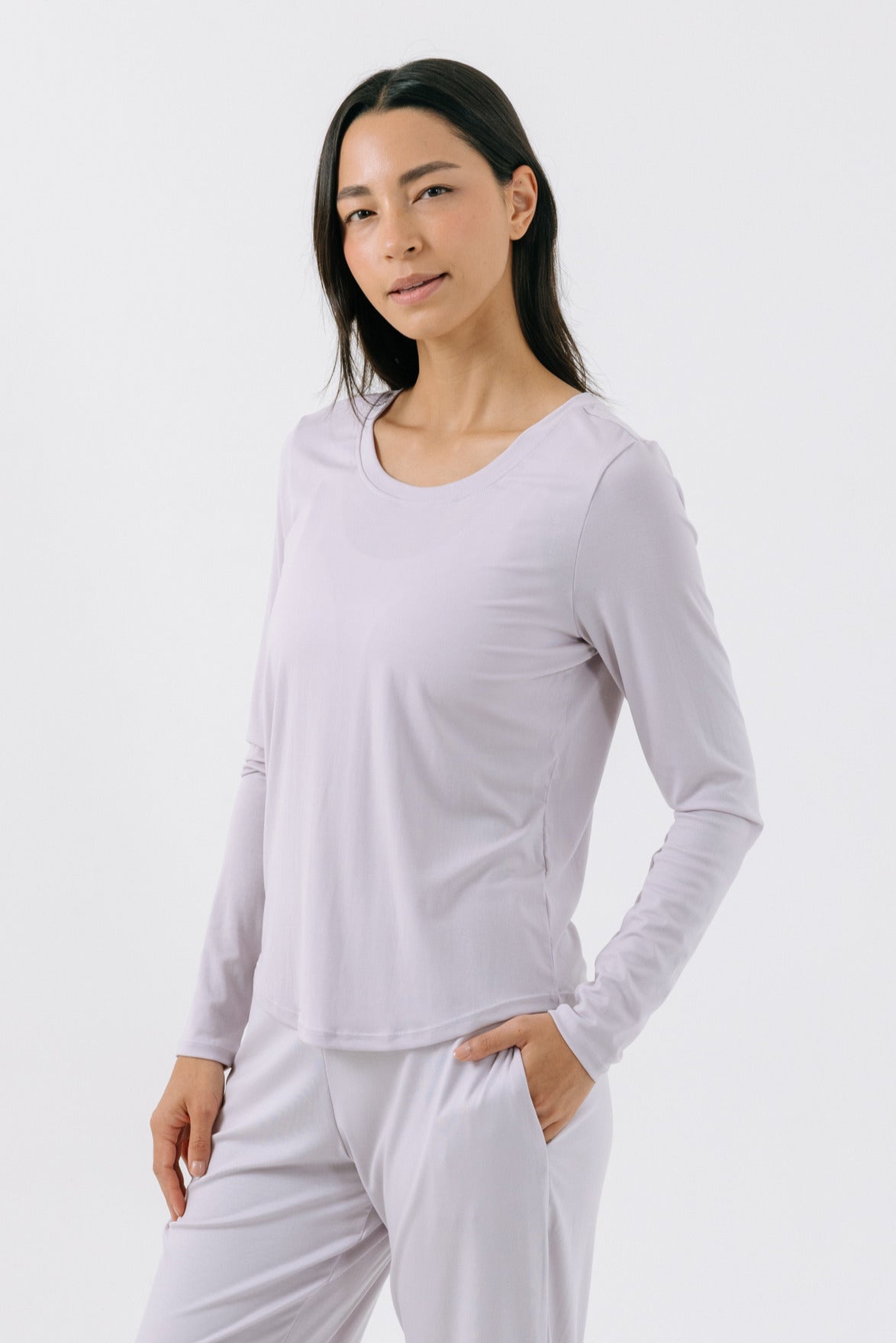 A woman wearing a lavender long-sleeve pajama t-shirt on a white, studio background.