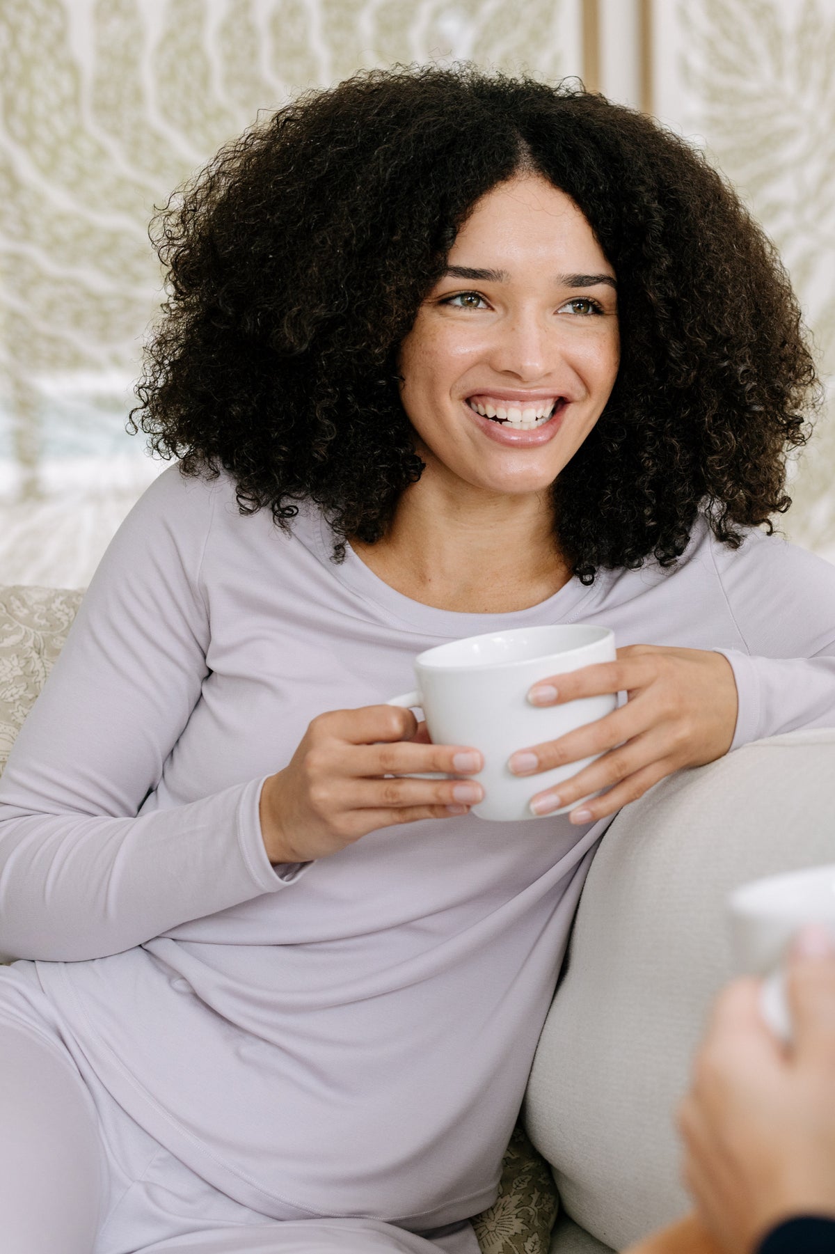 A woman wearing a lavender, long-sleeve pajama t-shirt holding a white coffee mug.