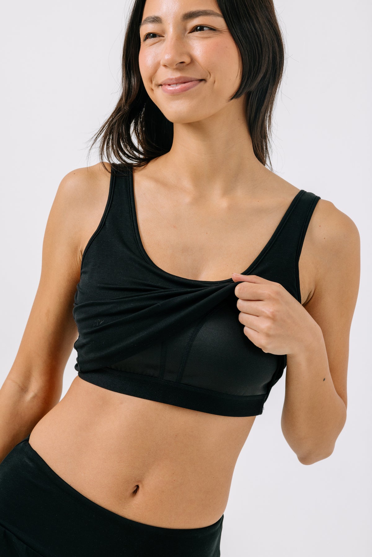 Woman wearing a black pajama crop top and showing a black built-in bra underneath on a white studio background.
