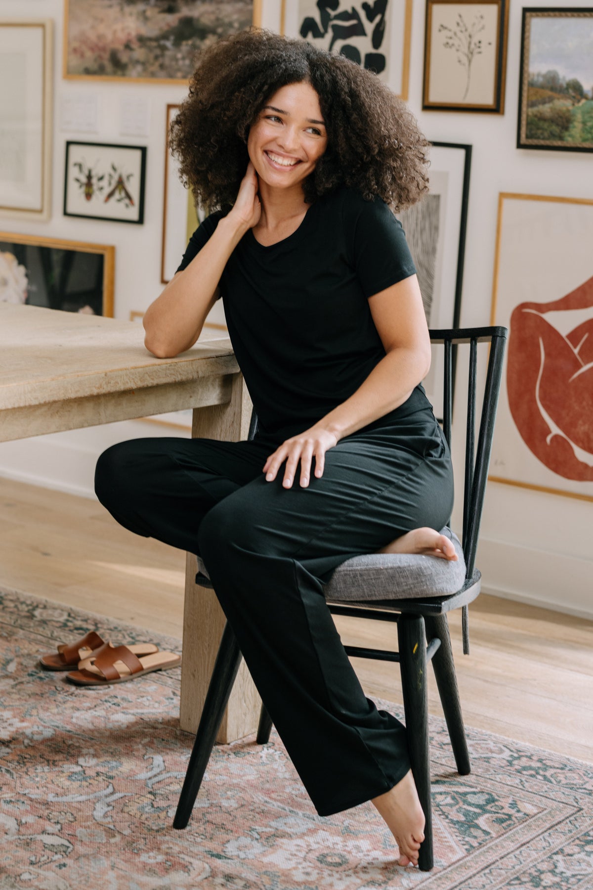 Woman sitting on a chair at a table wearing a black pajama t-shirt and matching black pajama pants. 