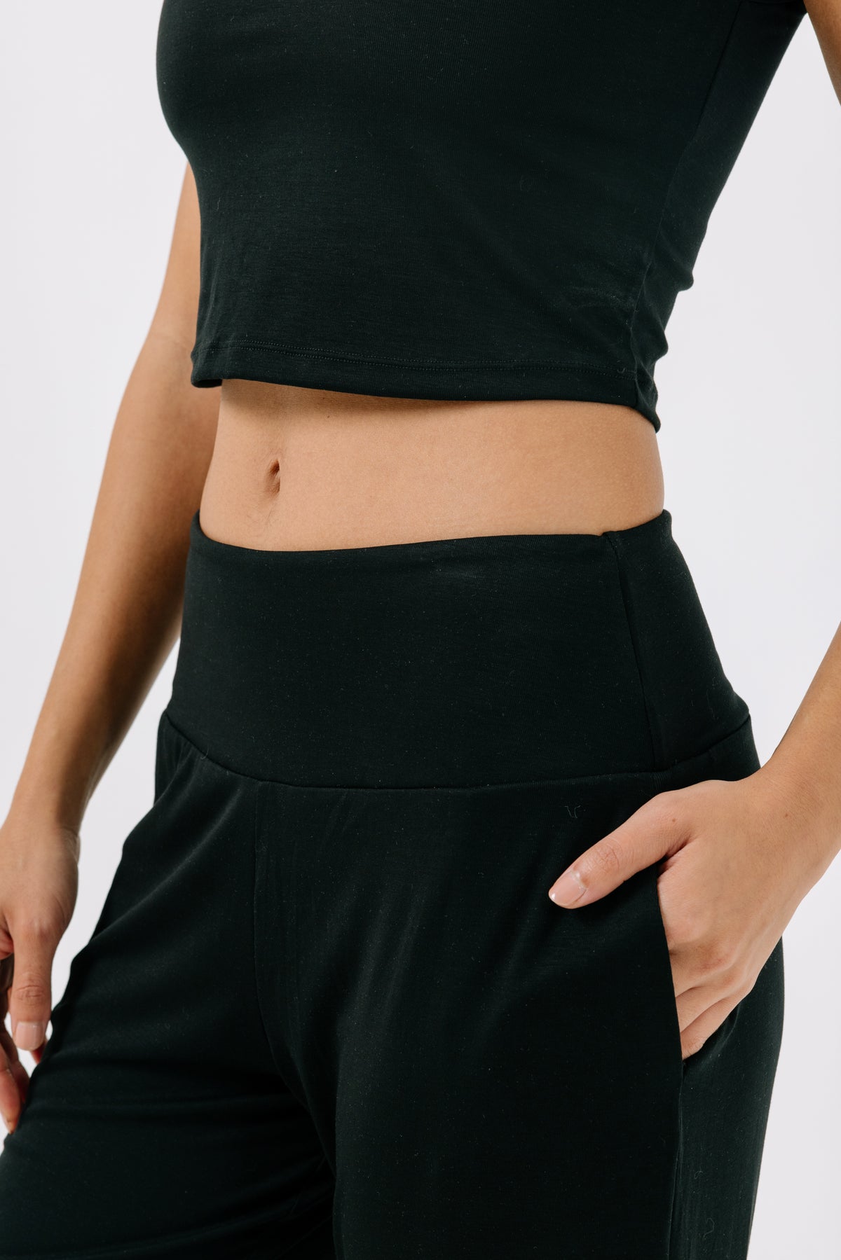 Woman wearing black pajama pants with her hand in her pocket on a white studio background.