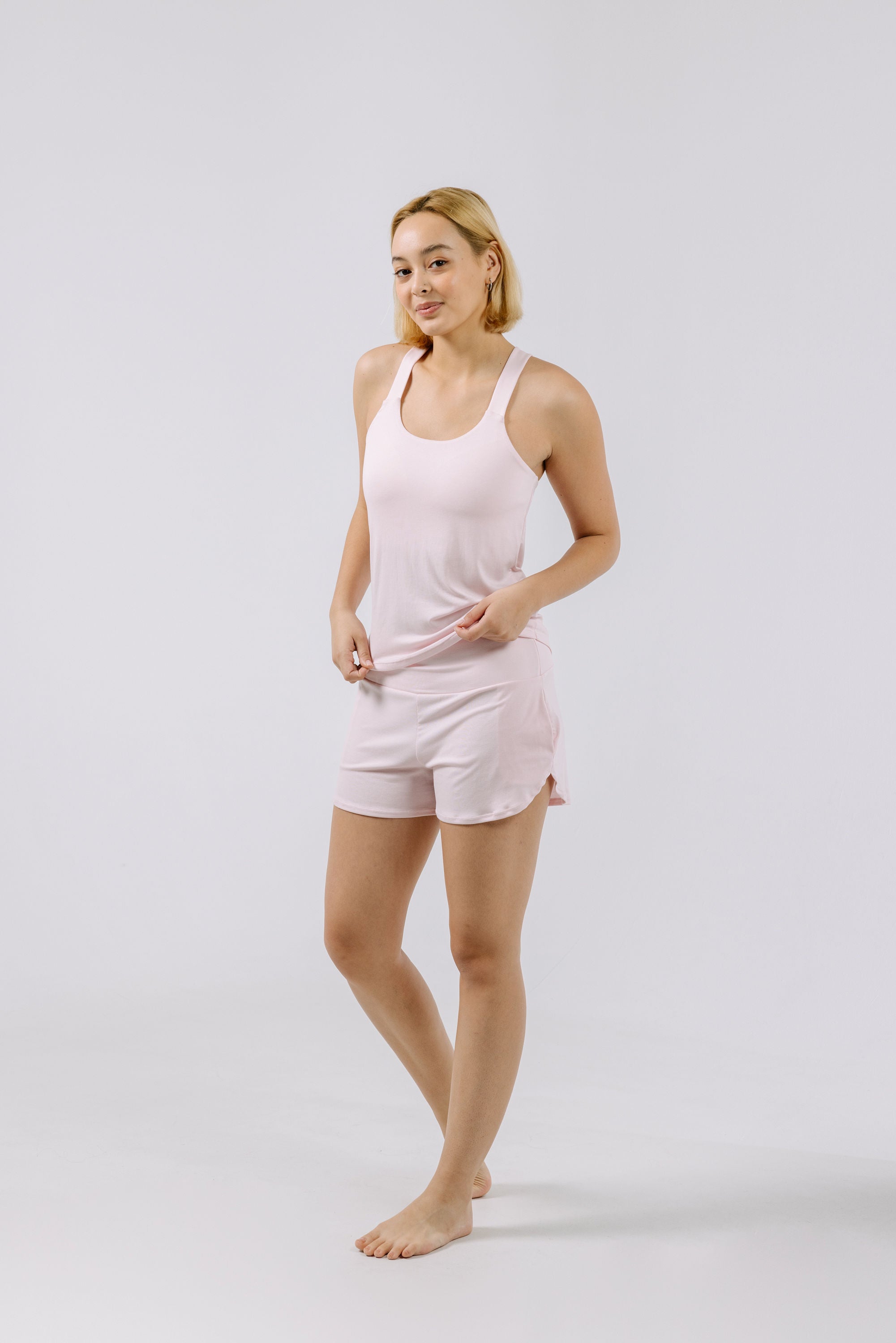 Woman wearing a pink pajama tank top and shorts on a white background.