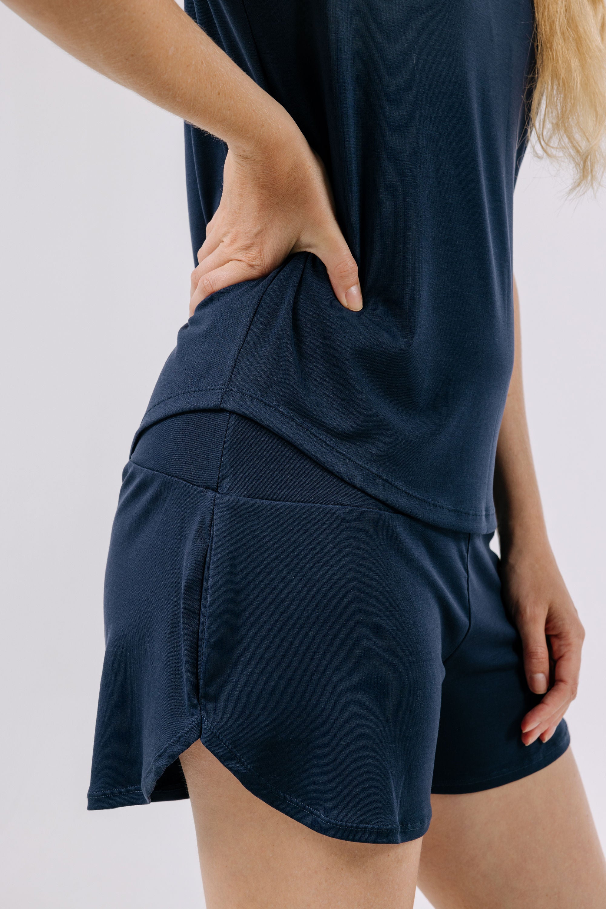 Person wearing a navy blue pajama t-shirt and shorts on a light gray background.