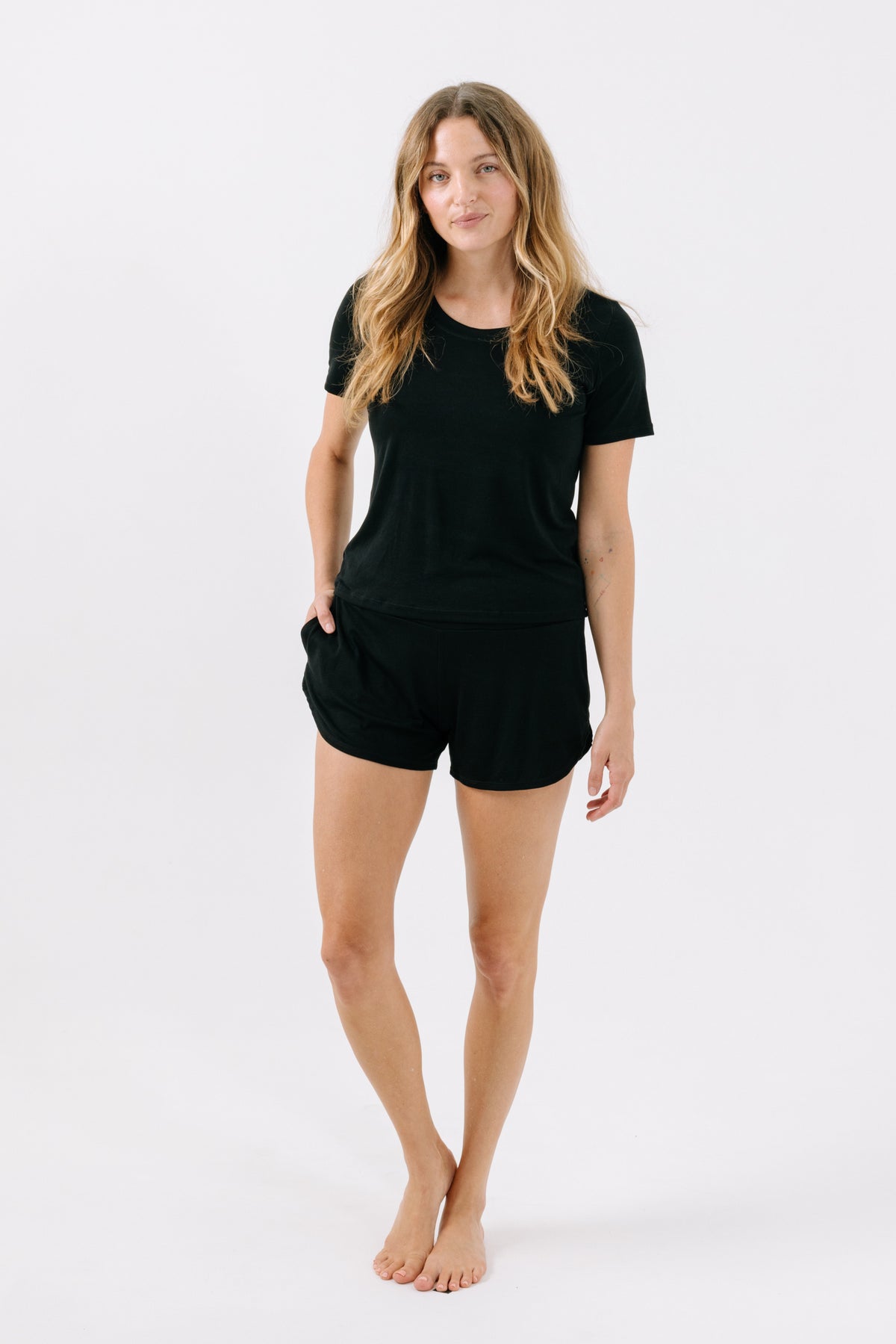 Woman wearing a matching black pajama t-shirt and shorts on a white studio background. 