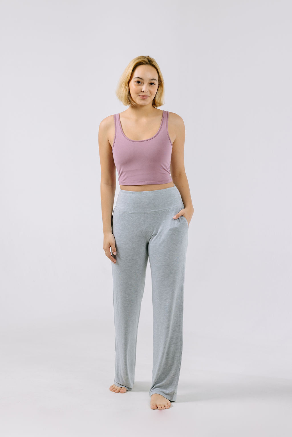 Woman wearing a dusty lilac pajama crop top and gray pajama pants on a white background.