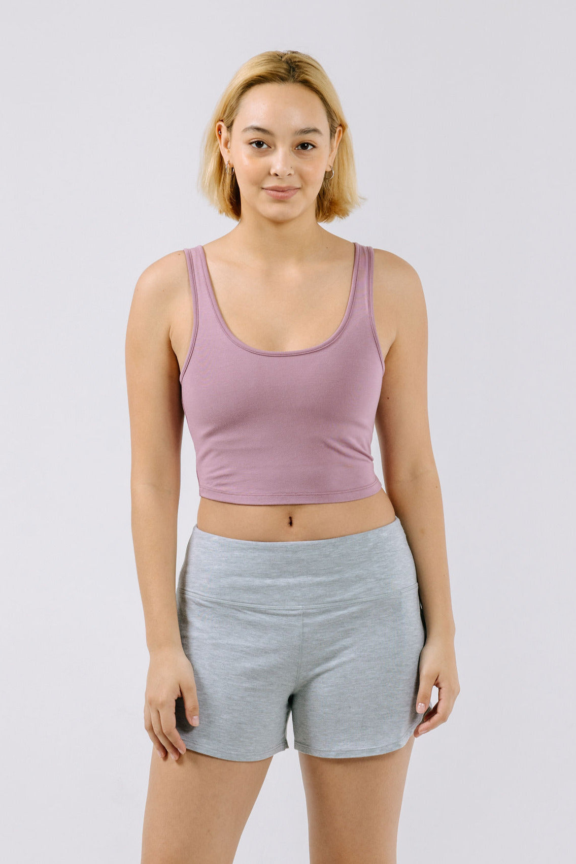 Woman wearing a dusty lilac pajama crop top and gray shorts on a white background.