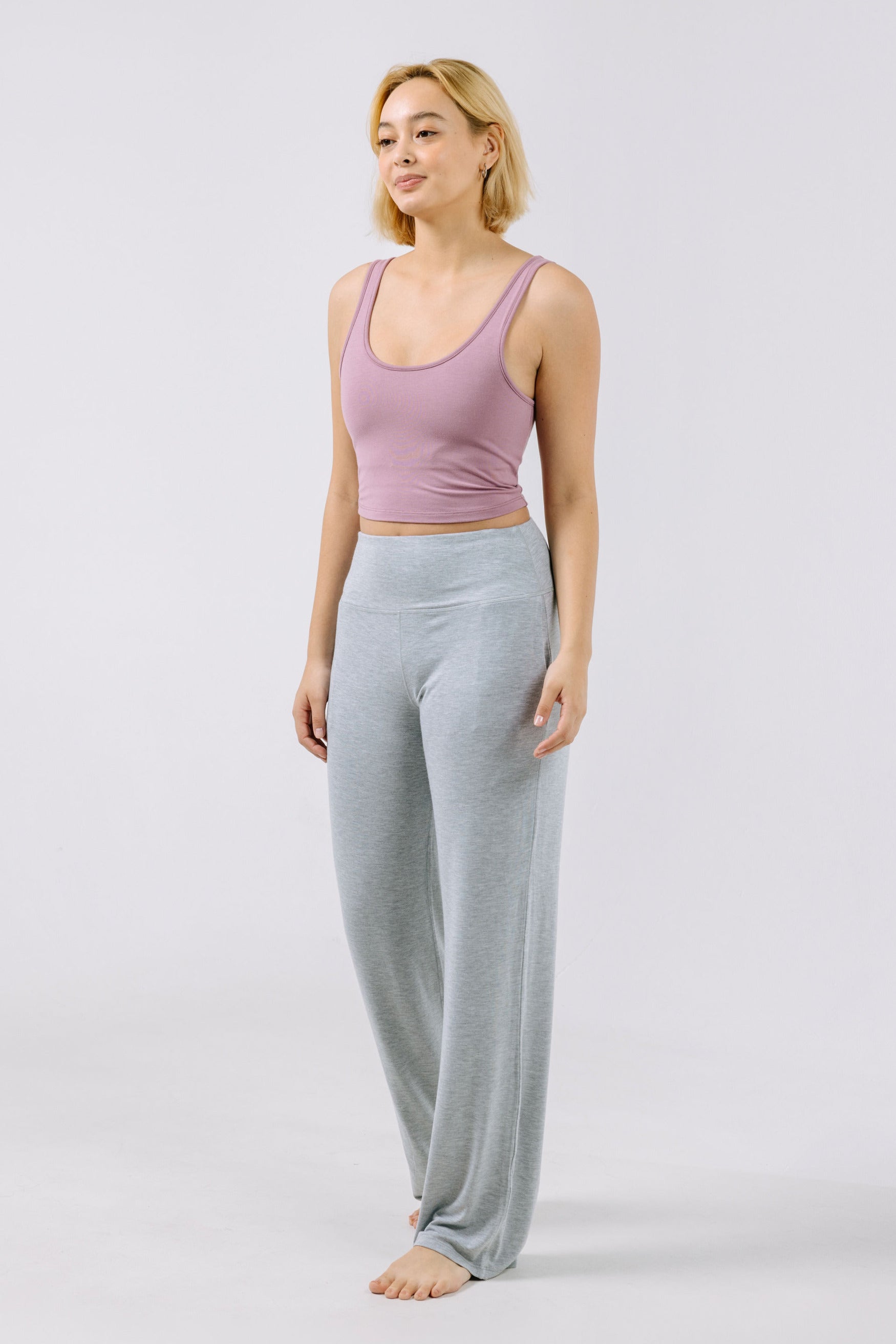 Woman wearing a dusty lilac pajama tank top and gray pajama pants on a white background.