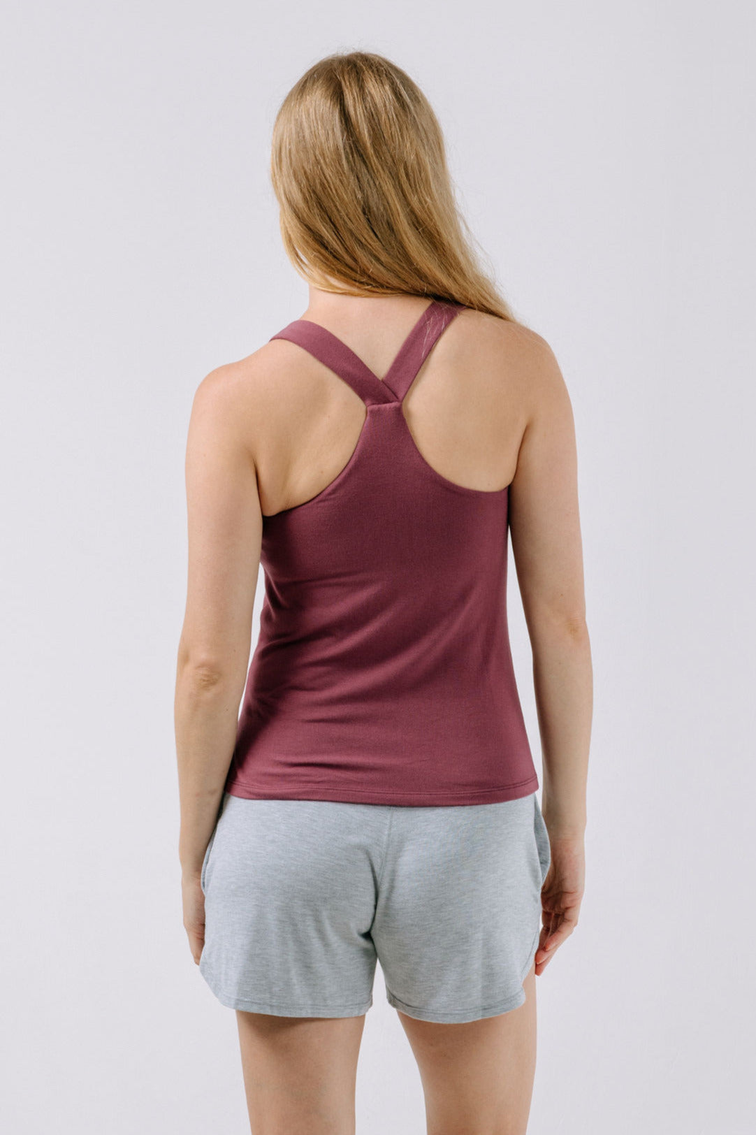 Woman wearing a plum pajama racerback tank top and gray shorts on a light gray background.