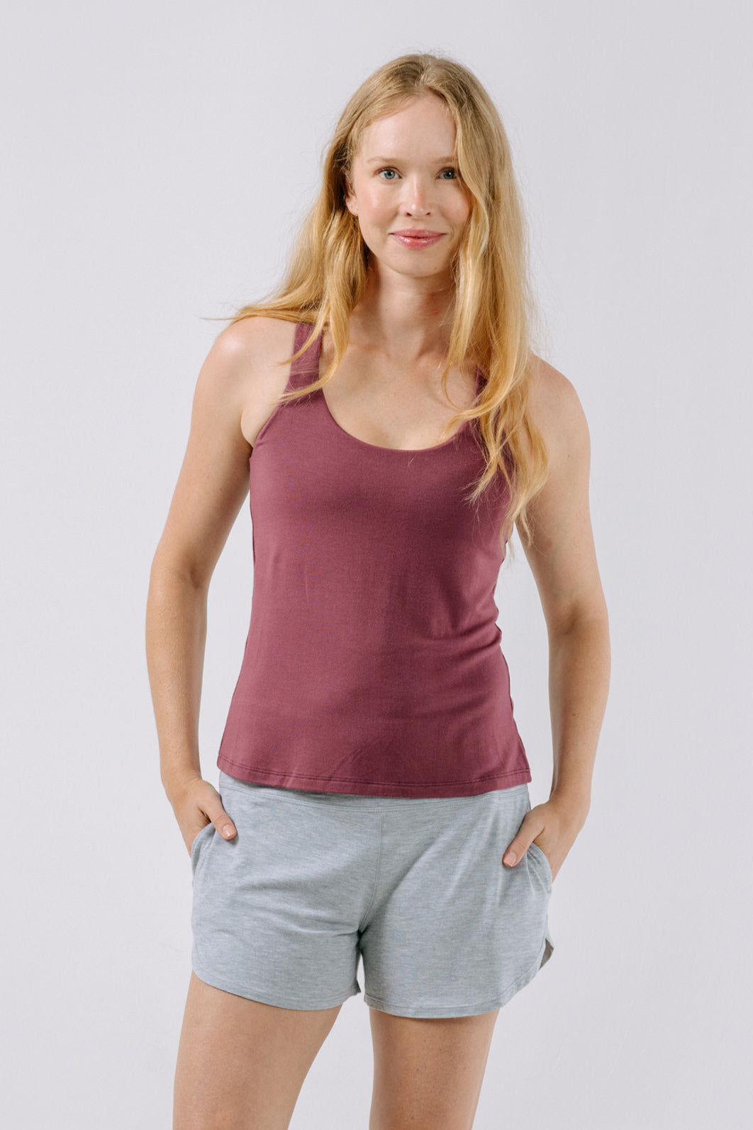Woman wearing a plum pajama tank top and gray shorts on a light gray background.