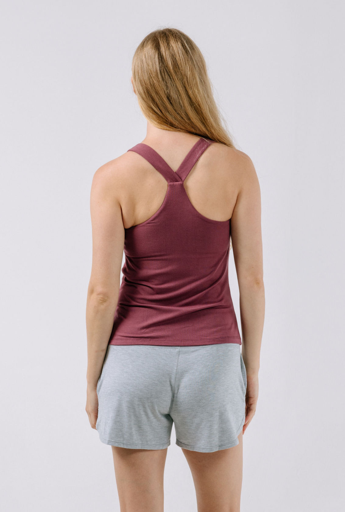 Woman wearing a plum pajama tank top and gray shorts on a light gray background.