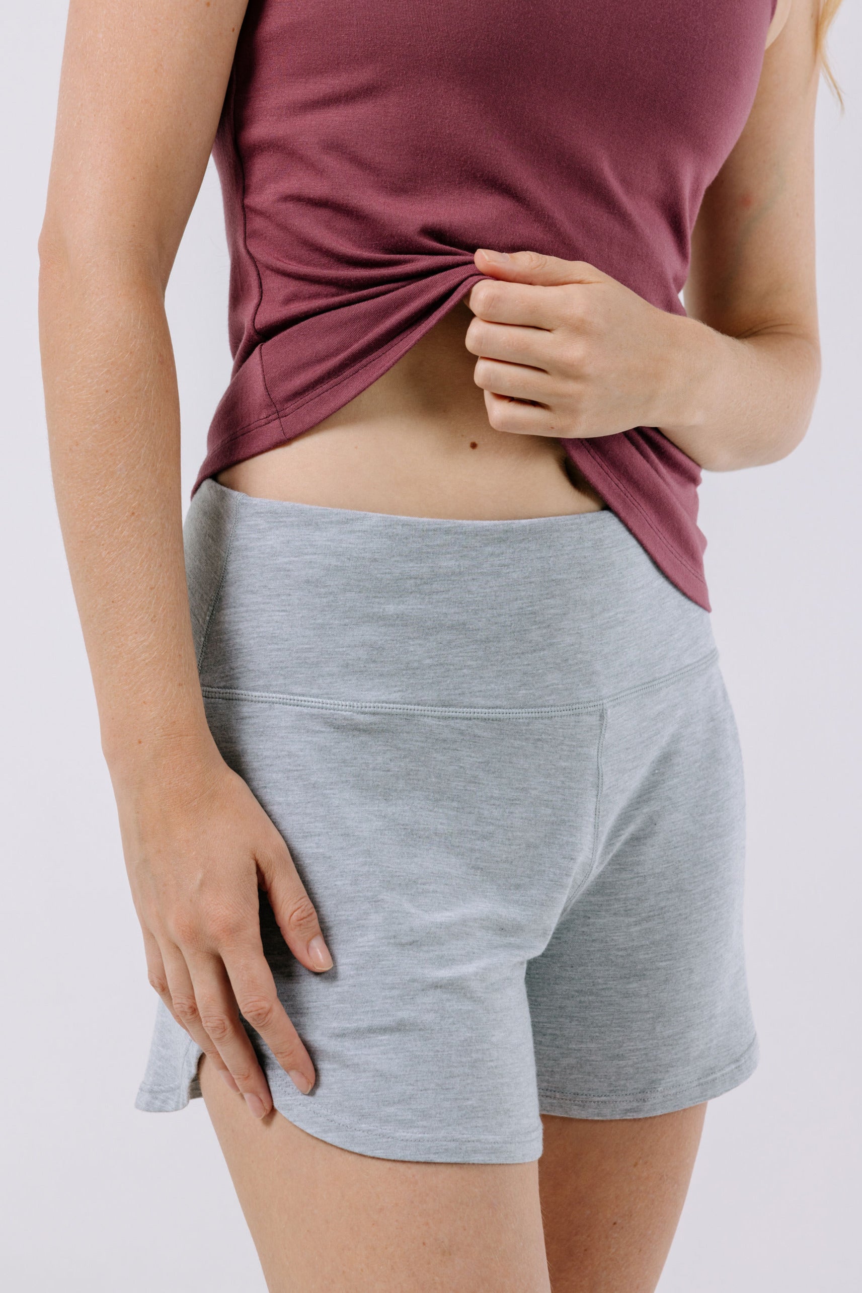 Person wearing a plum pajama top and gray shorts on a white background.