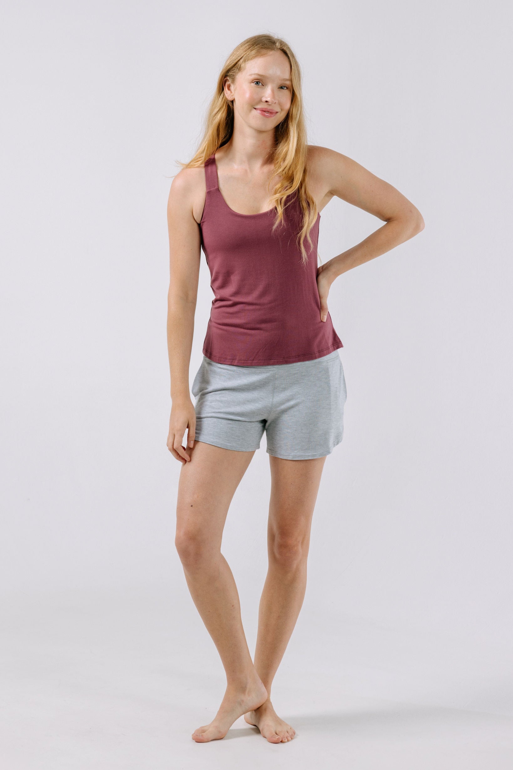 Woman wearing a plum pajama tank top and gray shorts on a white background.