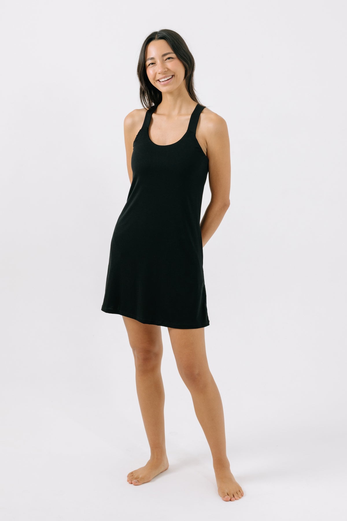 Woman wearing a black racerback pajama dress on a white background.